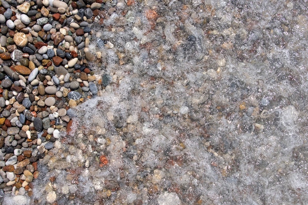 Pedras de seixo na praia do mar. As ondas ondulantes do mar com espuma