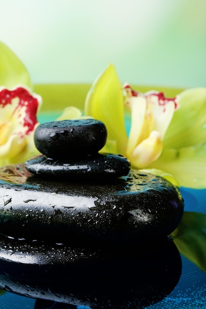 Pedras de spa com gotas de água e belas orquídeas florescentes na água em fundo natural
