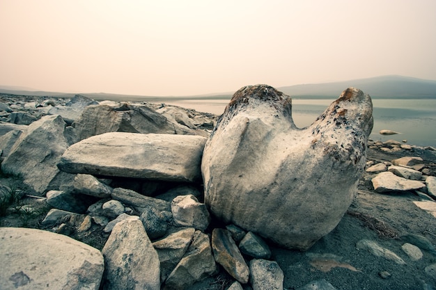 Foto pedregulhos enormes à beira do lago em manhã de nevoeiro