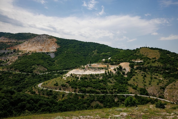 Pedreira para extração de minerais com equipamentos e máquinas e estrada nas montanhas Rhodope cobertas de florestas