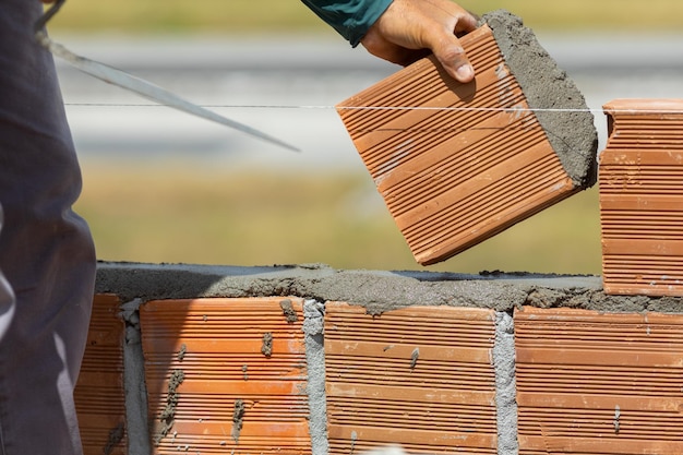 pedreiro instalando tijolo na parede externa. Trabalhador da construção civil profissional colocando tijolos.