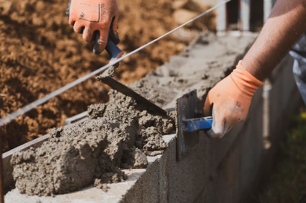 Pedreiro na luva espalhando concreto para construir uma parede no canteiro de obras