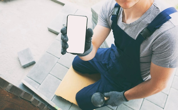 Foto pedreiro segurando o telefone com tela em branco na mão na maquete de luvas para reparo ou construção de casas