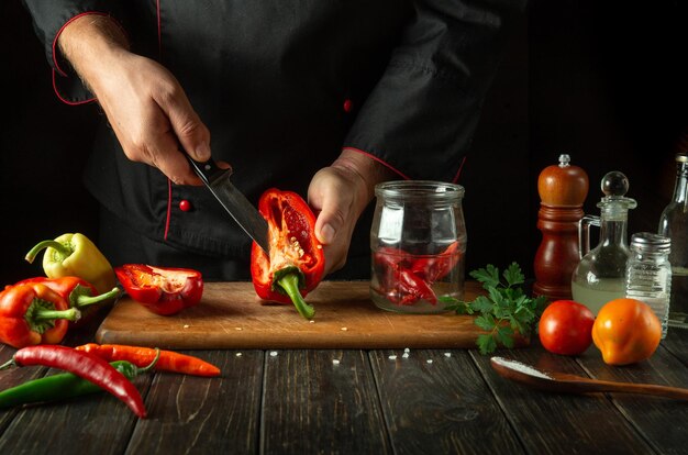 Peeling capsicums antes de cortar para enlatar em um frasco Mãos de chefs com uma faca e uma fatia de pimenta em uma cozinha de restaurante