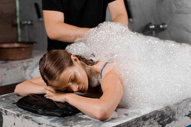 Peeling de espuma em hammam de spa turco. Modelo atraente é relaxante no spa. Massagista está fazendo massagem com luva de esponja.