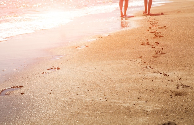 Pegadas de praia, onda e mulheres ao pôr do sol tempo com sol flare