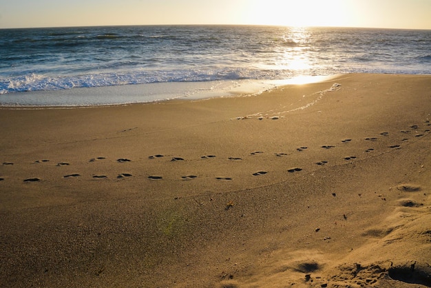 Pegadas em uma praia limpa de areia do mar paralela à costa Ondas espirram na costa