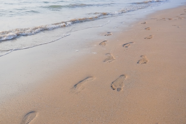 Pegadas na areia ao pôr do sol. praia tropical com ondas do mar