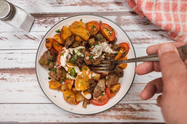 Pegando à mão uma porção de pedaços de carne refogados com mandioca ou mandioca cebolinha pimenta limão e tomate cereja em uma superfície rústica