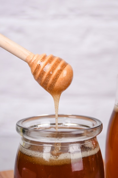 Foto pegue o mel de um recipiente de vidro usando uma ferramenta de madeira