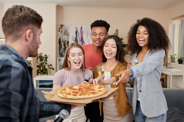 Pegue uma fatia de pizza amigos multiculturais entusiasmados com pizza recém-assada enquanto se divertem no karaokê