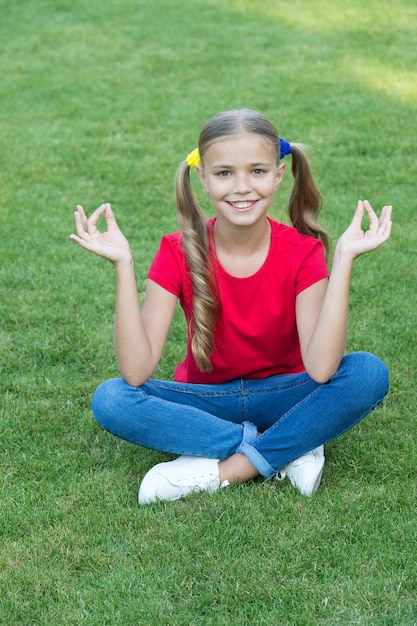 Peinado de cola de caballo lindo de niña relajante sobre la hierba verde, practicar el concepto de meditación.