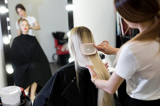 Peinar el cabello. El maestro de peluquería prepara a la niña del cliente para restaurar los procedimientos.