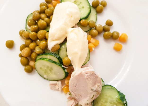 Peito de frango cozido com ervilhas verdes cozidas, pepino e molho em um prato branco. nutrição saudável e equilibrada, o conceito de dieta