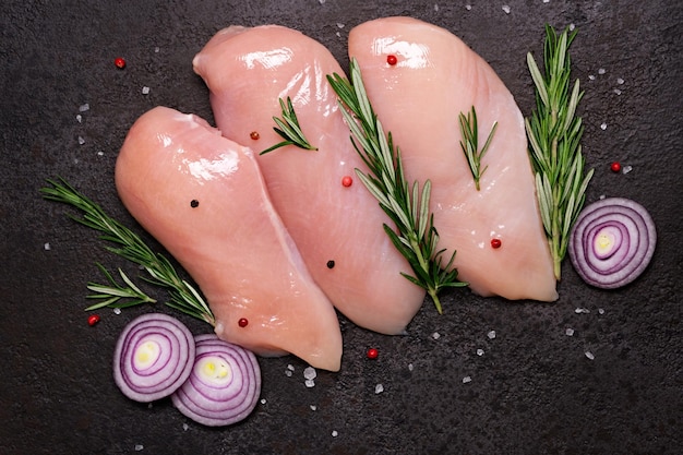 Peito de frango cru com especiarias e ervas em fundo de pedra preta Preparação para cozinhar