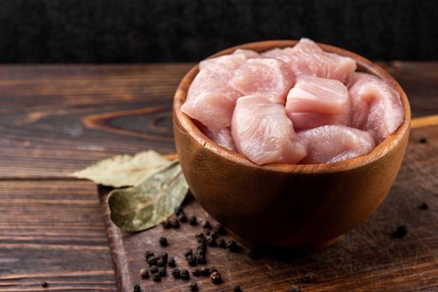 Peito de frango cru em cubos ou filetes no fundo escuro de madeira.