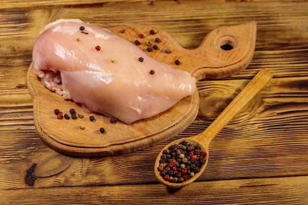 Peito de frango cru na tábua de cortar na mesa de madeira