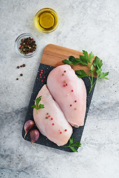 Peito de frango Dois filé de frango com especiarias azeite e salsa na tábua de pedra preta no fundo da mesa de pedra cinza Vista superior com espaço de cópia Fundo de cozimento de carne de comida