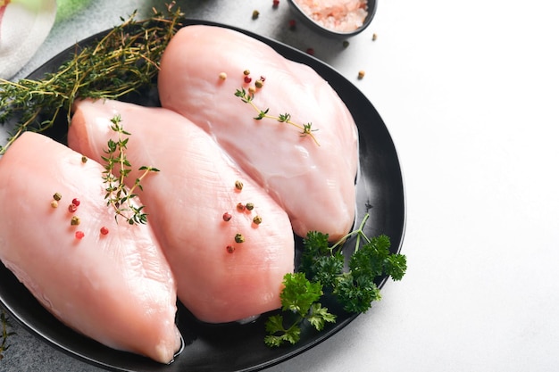 Peito de frango Filetes de peito de frango cru na placa de cerâmica preta na tábua de madeira com ervas e especiarias no fundo da velha mesa cinza Vista superior com espaço de cópia