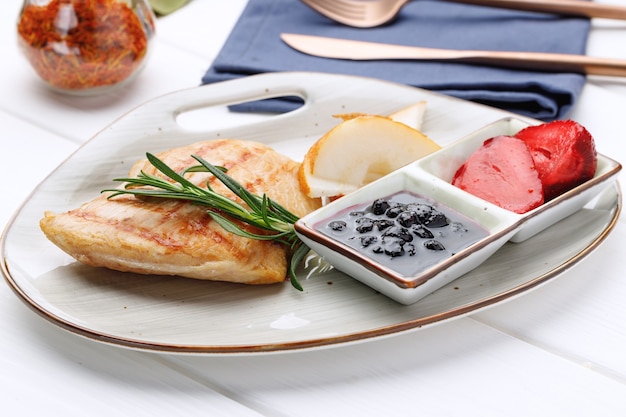 Peito de frango grelhado com molho de frutas vermelhas no prato na mesa de madeira branca fechada