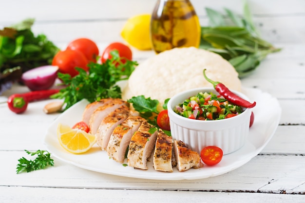 Peito de frango grelhado com molho de tomate fresco e pão árabe.