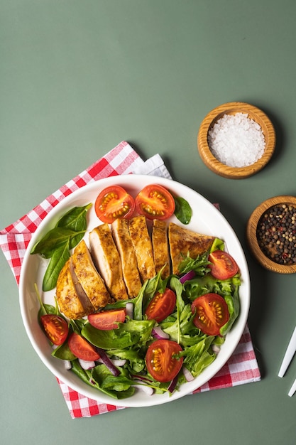 Peito de frango grelhado com salada verde de salada de legumes fresca de alface, rúcula, espinafre, pepino e tomate no prato na mesa cinza. Menu de almoço saudável. Fundo de comida de dieta. Vista do topo