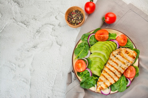 Peito de frango grelhado e salada de legumes fresca com folhas de espinafre, abacate e tomate em um fundo claro. salada de verduras com carne. o conceito de dieta alimentar. copie o espaço. banner de comida.