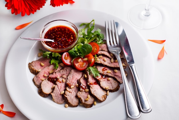 Peito de pato assado com tomate, espinafre com molho de baga em um prato branco