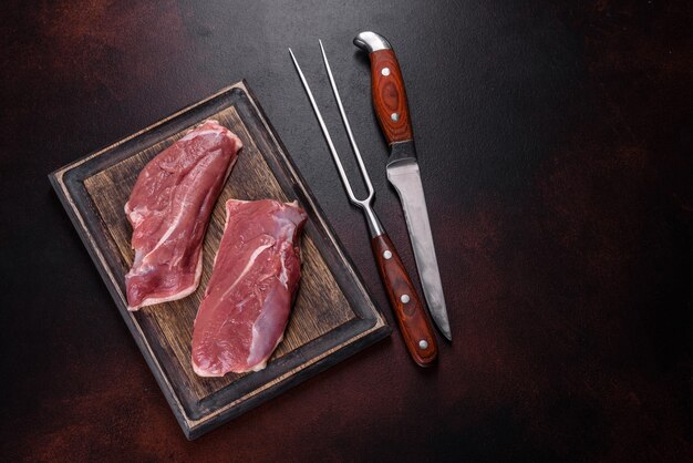 Peito de pato cru com ervas e especiarias em um fundo escuro de concreto. carne crua preparada para assar