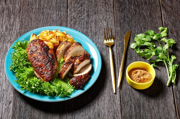 Peitos de frango condimentados com cubos de ananás grelhados e alface de folhas verdes frescas em um prato azul sobre uma mesa de madeira