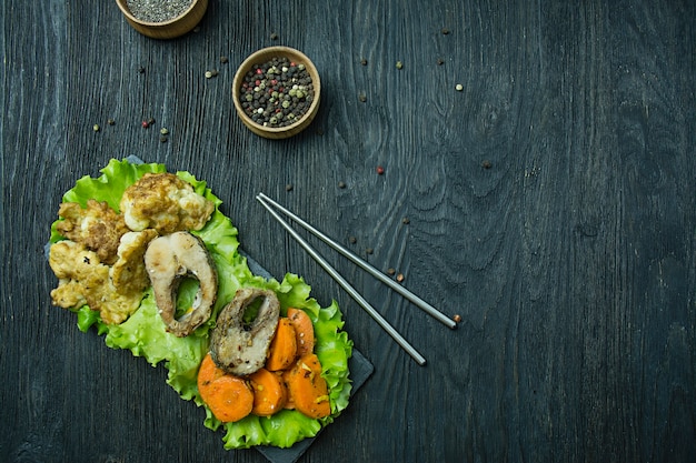 Peixe assado com legumes. fishplate. nutrição apropriada. comida ecológica. fundo escuro. espaço para texto.