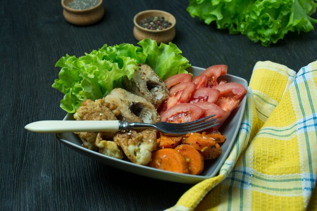 Peixe assado com legumes. Fishplate. Nutrição apropriada. Comida ecológica. Fundo escuro.