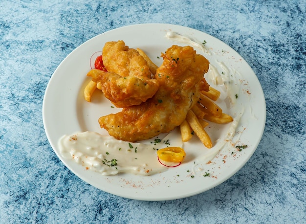 Peixe batido com batatas fritas, limão e molho servido em prato isolado no fundo, vista superior da comida italiana