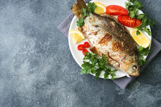 Peixe carpa assada com legumes e especiarias em um prato sobre uma mesa escura