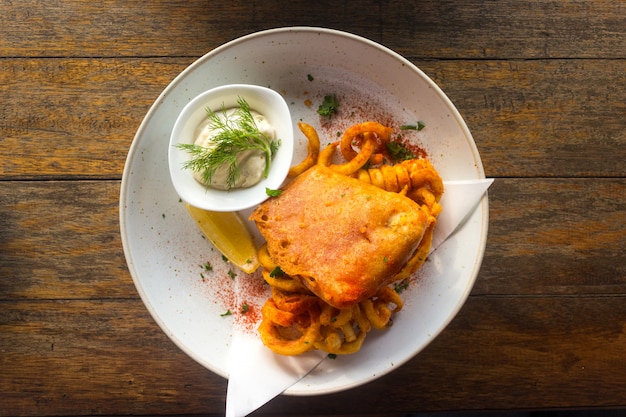 Peixe com batatas fritas com molho tártaro em um prato sobre uma mesa de madeira