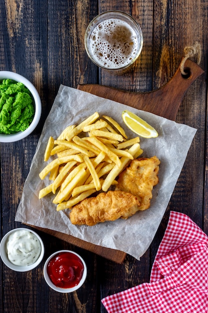 Peixe com batatas fritas em um fundo de madeira. Fast-food britânico. Receitas. Lanche de cerveja. Cozinha inglesa.