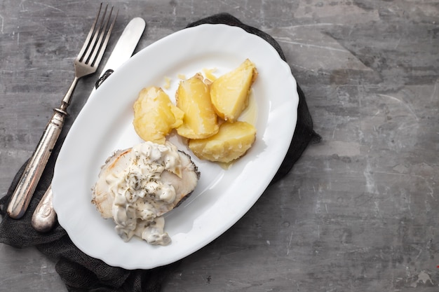 Peixe cozido com molho de tártaro e batata cozida no prato branco na mesa de cerâmica