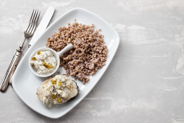 Peixe cozido com trigo sarraceno e molho no prato branco na mesa de cerâmica