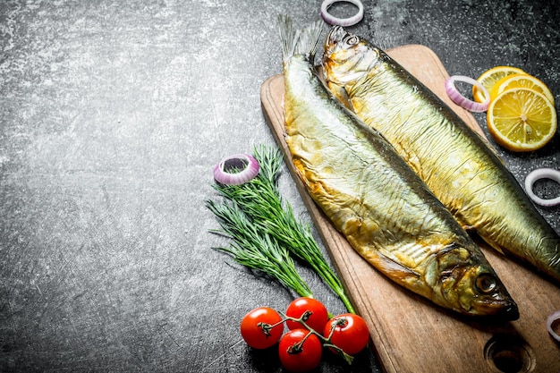 Peixe defumado em uma tábua de corte de madeira com endro de tomate e rodelas de limão