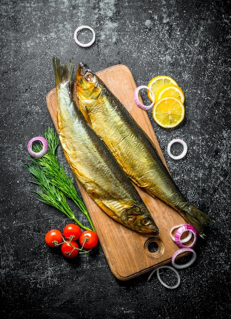 Peixe defumado em uma tábua de corte de madeira com endro de tomate e rodelas de limão