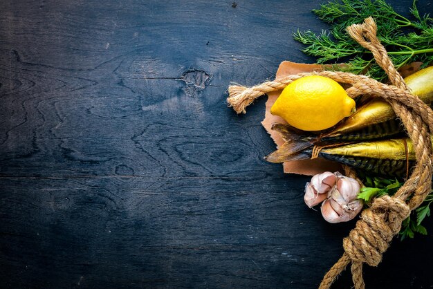 Peixe defumado na tábua de madeira com legumes frescos em um fundo preto de madeira vista superior