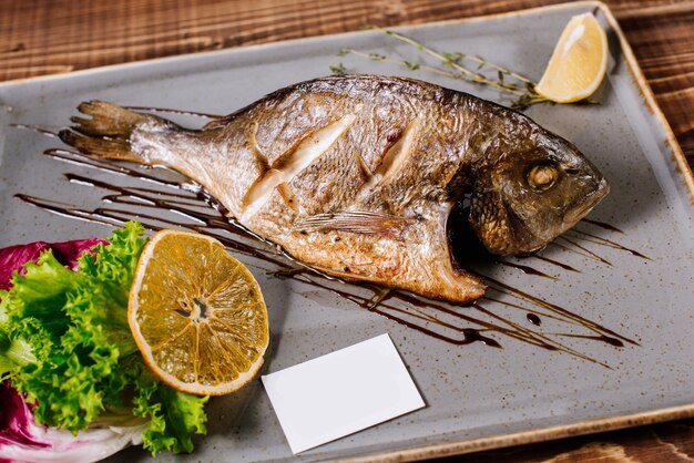 Peixe dourado defumado com ervas em fundo de madeira