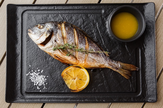 Peixe dourado delicioso dorado ou pargo com rodelas de limão, especiarias, alecrim na pedra escura.