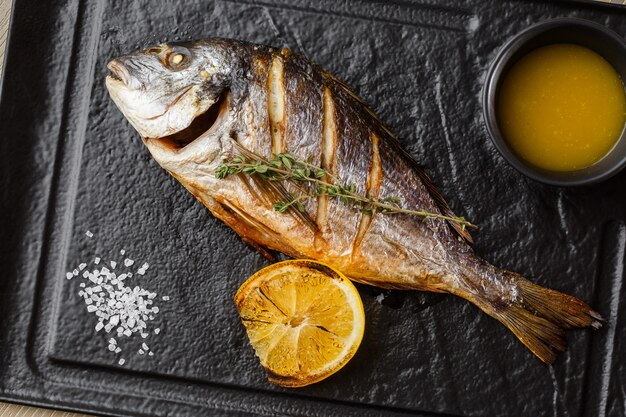 Peixe dourado delicioso dorado ou pargo com rodelas de limão, especiarias, alecrim na pedra escura.