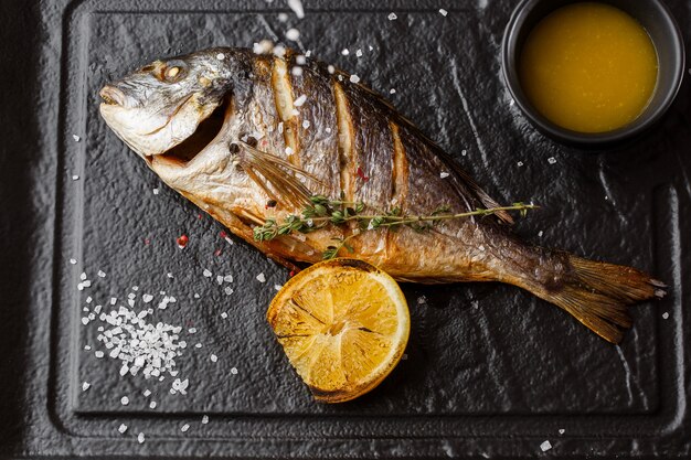 Peixe dourado delicioso dorado ou pargo com rodelas de limão, especiarias, alecrim na pedra escura.