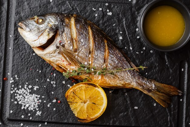 Peixe dourado delicioso dorado ou pargo com rodelas de limão, especiarias, alecrim na pedra escura.