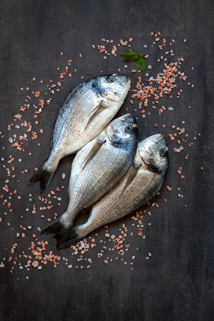 Peixe dourado fresco com sal rosa na tábua de corte preta sobre a mesa