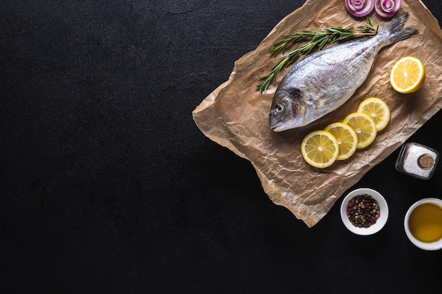 Peixe dourado fresco cru no papel de cozinha preparado para cozinhar com especiarias em um fundo preto. Frutos do mar. Vista do topo. Copie o espaço.