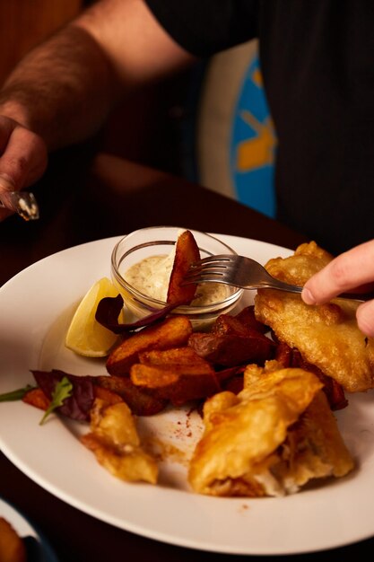 Foto peixe empanado em um prato com batatas fritas em uma mesa de madeira em comida insalubre de pub