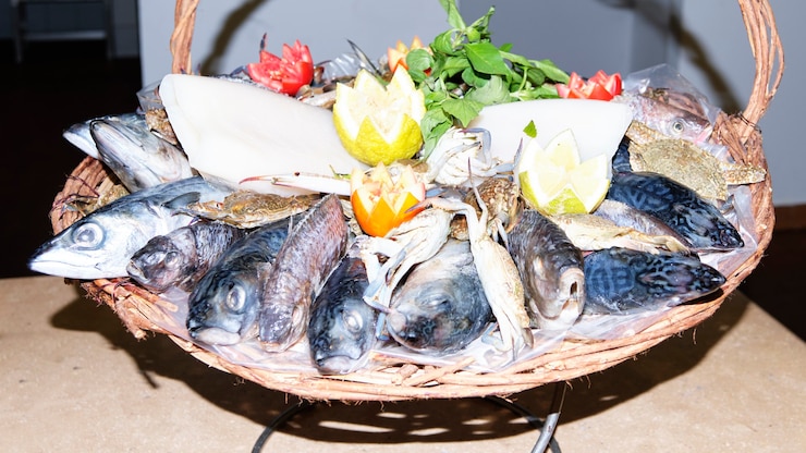 Foto peixe fresco colocado em uma cesta decorada com limão, tomate e ervas.